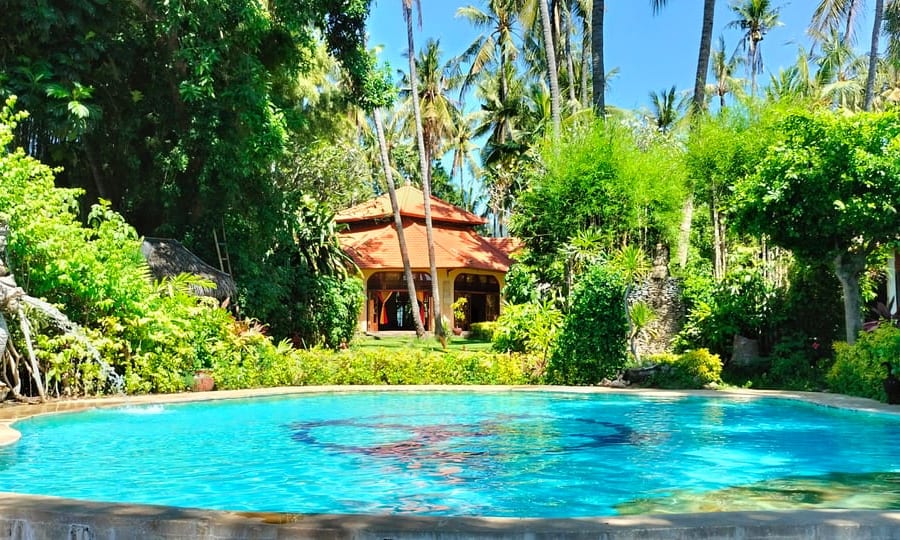 Bali-Mandala-Meditationshalle — ein achteckiger Pavillon mit Palmblattdach inmitten tropischer Gärten, davor der Quellwasserpool mit dem Bali-Mandala-Motiv